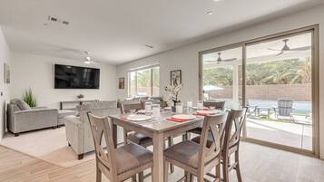 A modern living room with a dining table, chairs, sofas, and a TV mounted on the wall.