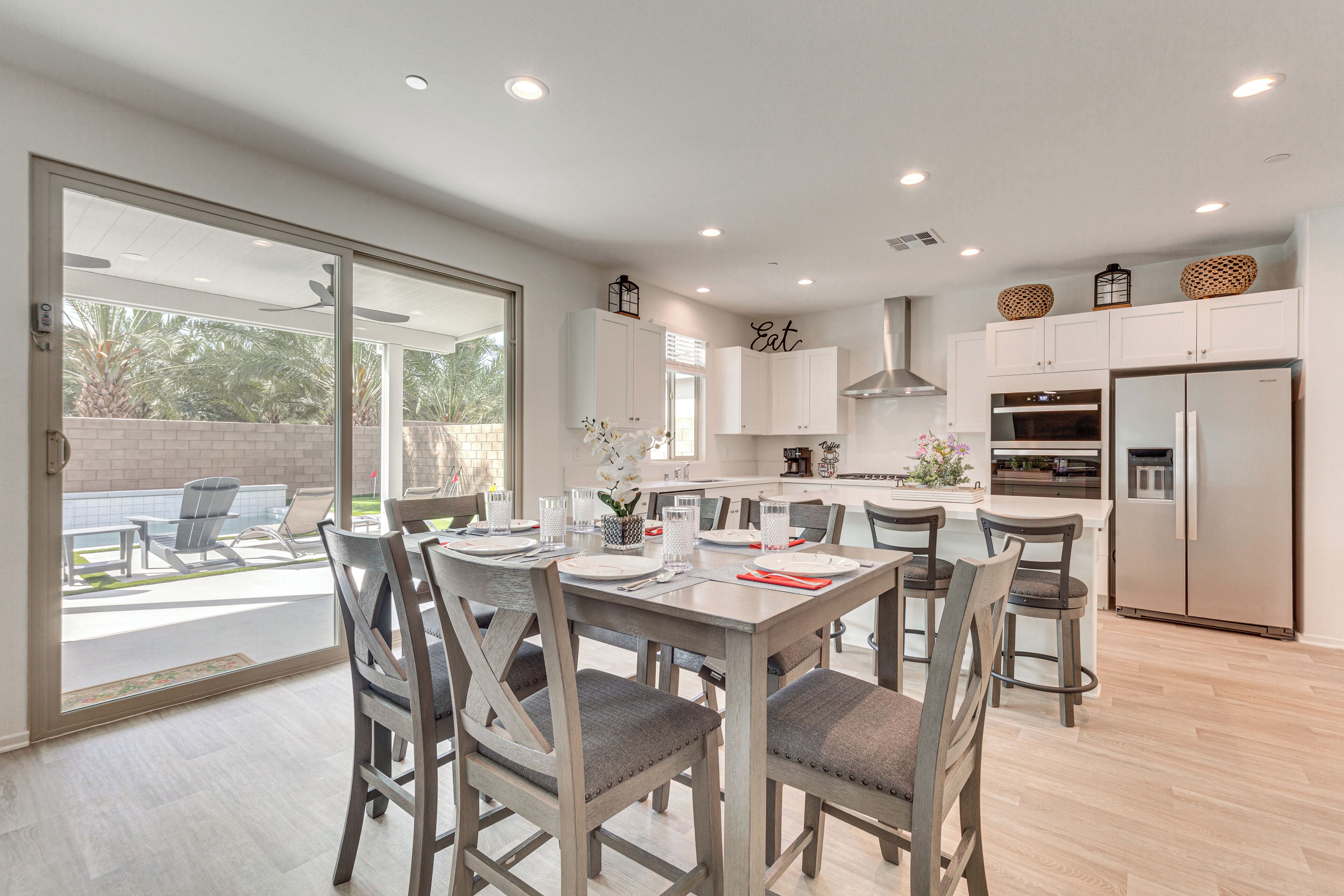 A modern kitchen with white cabinets, a stainless steel refrigerator, and a dining area with grey chairs and a table set for four.