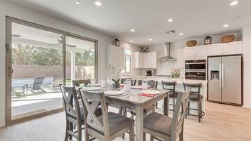 A modern kitchen with white cabinets, a stainless steel refrigerator, and a dining area with grey chairs and a table set for four.