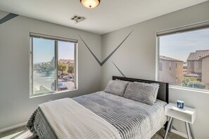 A bedroom with a bed, two windows, a bedside table, and a view of the street. - Big Yard & Patio! Modern Home Near Vegas Strip (Las Vegas)