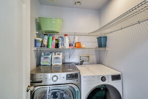 A laundry area with two washing machines, shelves with cleaning supplies, and a green basket. - Big Yard & Patio! Modern Home Near Vegas Strip (Las Vegas)