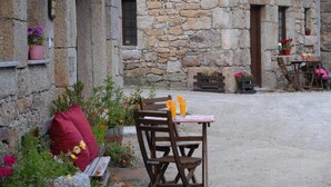 A rustic stone building with a wooden bench, a table with chairs, and potted plants. - Casas Da Ribeira (Seia)