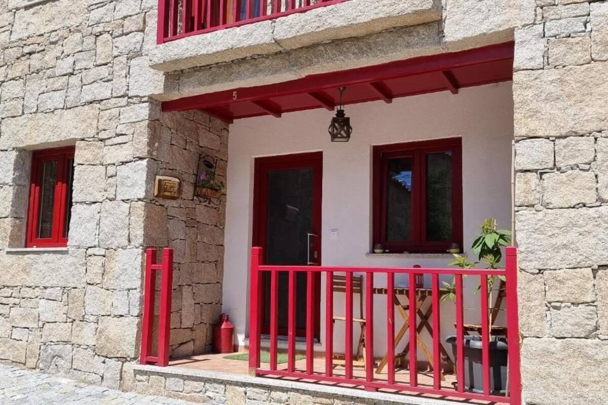 A stone building with a balcony, red railings, and a small table.