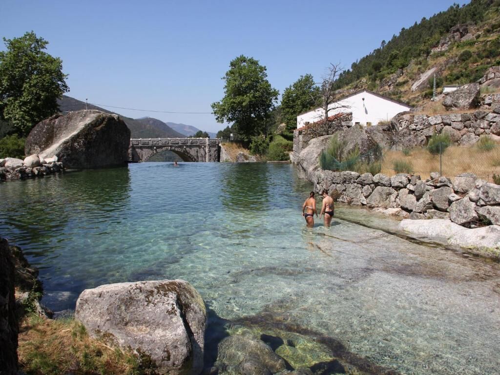 A clear water body with a stone bridge, rocky shore, and a white building with a stone wall.