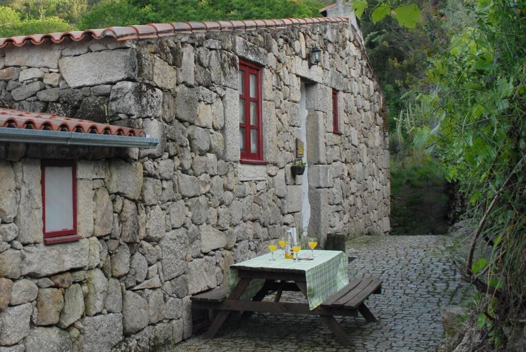 Un edificio de piedra con marcos de ventana rojos, un camino adoquinado y una mesa de picnic con mantel.
