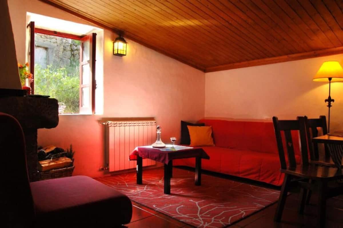 A cozy room with a red sofa, a wooden ceiling, a table with a lamp, and a window with a view.