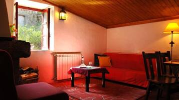 A cozy room with a red sofa, a wooden ceiling, a table with a lamp, and a window with a view.