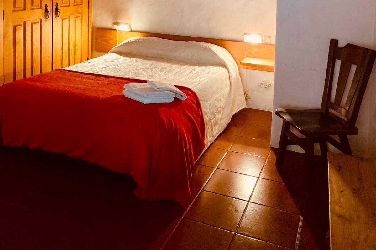 A bedroom with a bed, a chair, wooden ceiling, and a red blanket.