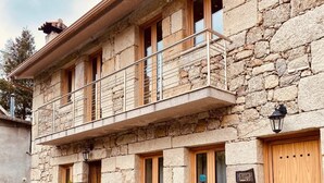A stone building with a balcony, wooden doors, and potted plants. - Casas Da Ribeira (Seia)