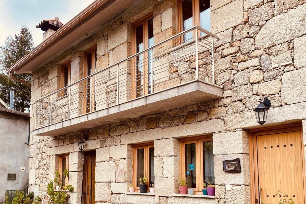 A stone building with a balcony, wooden doors, and potted plants.