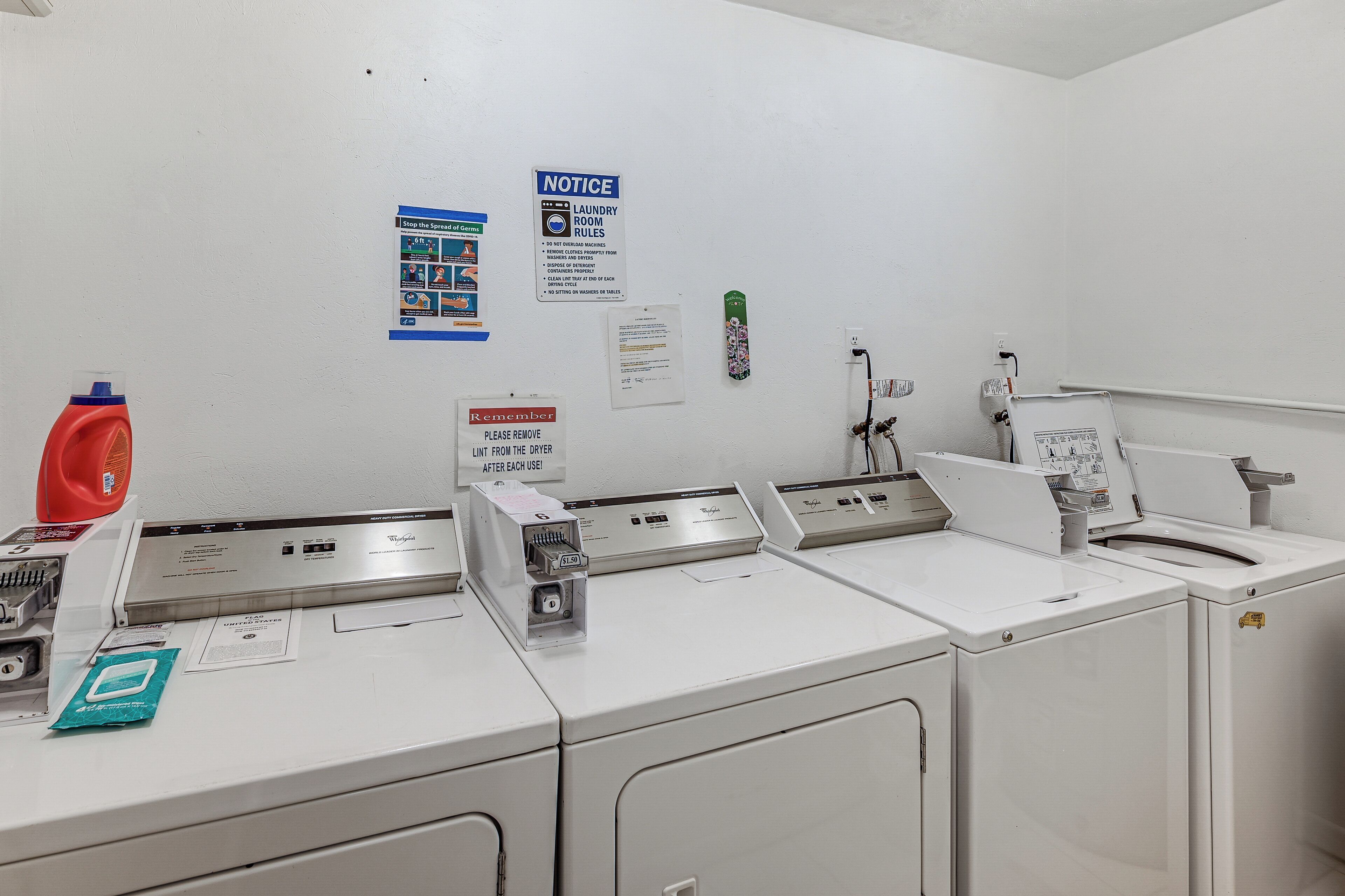 A laundry room with multiple washers and dryers, a notice board with laundry rules, and a detergent dispenser.