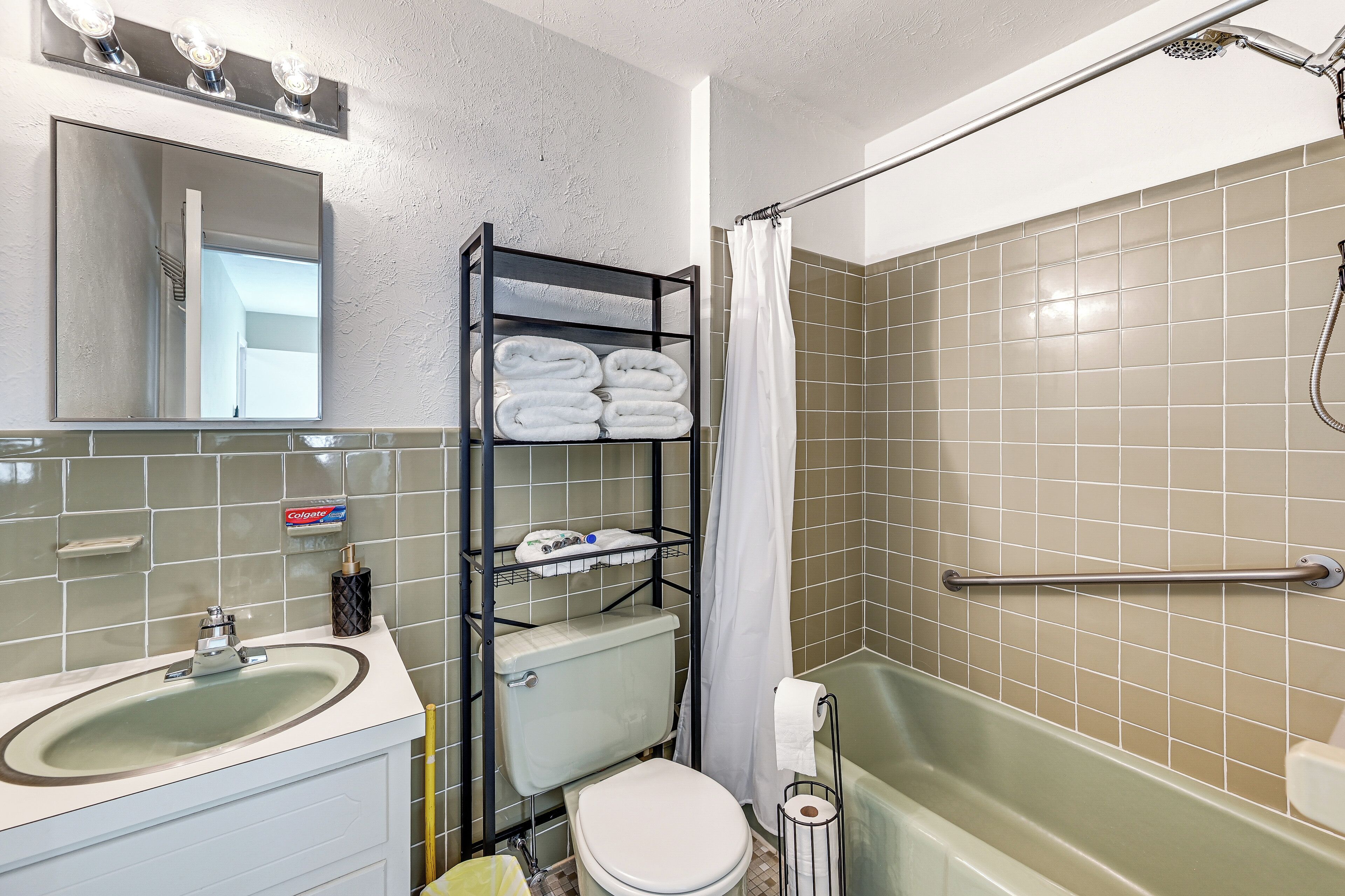 Une salle de bain avec un lavabo, des toilettes et une douche. On y trouve une étagère avec des serviettes et des articles de toilette.