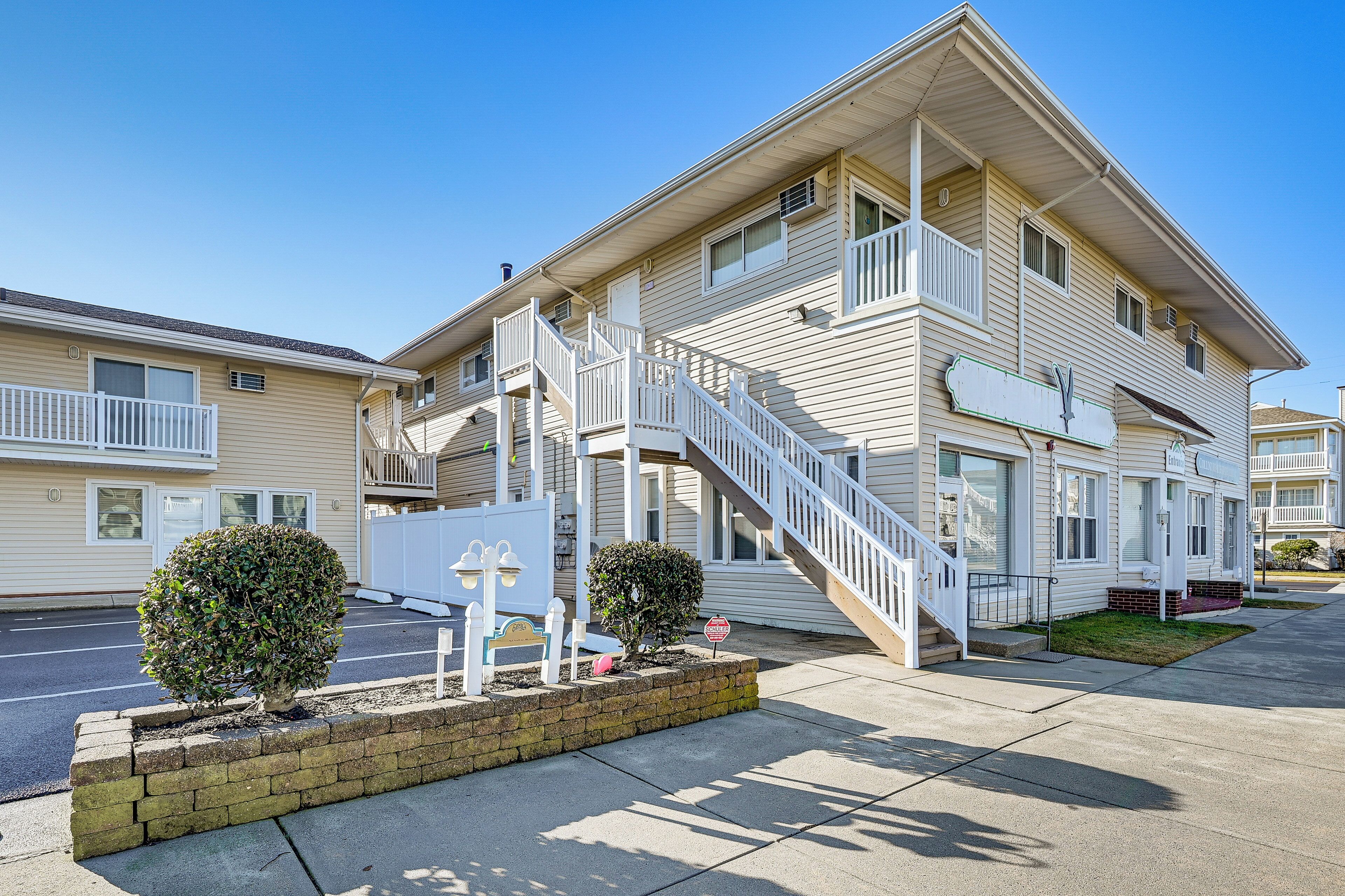 A two-story motel with a central staircase, a small front garden, and a clear sky.