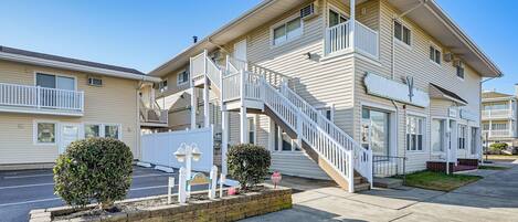 A two-story motel with a central staircase, a small front garden, and a clear sky.
