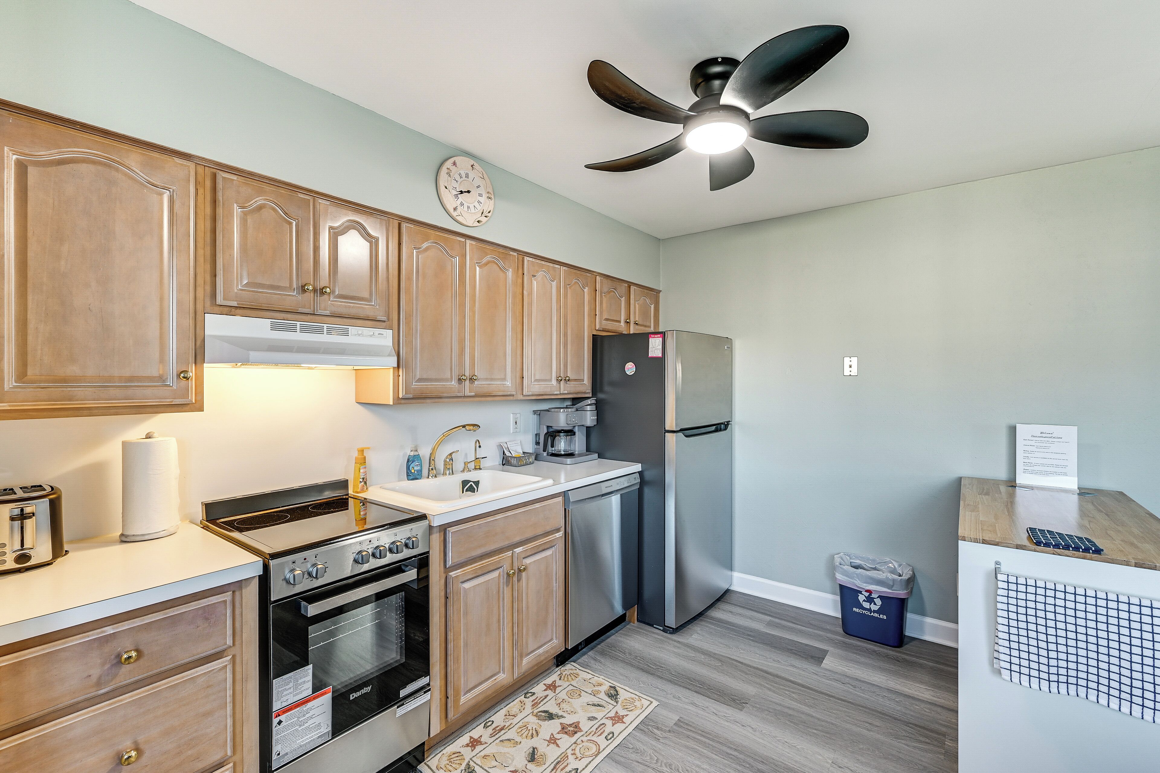 A kitchen with wooden cabinets, a stove, a refrigerator, and a ceiling fan.