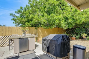 An outdoor kitchen area with a grill, a refrigerator, and a trash can.