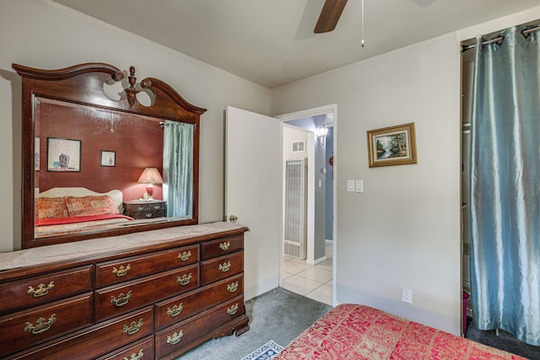 A bedroom with a wooden dresser, a bed with a red bedspread, a mirror, and a door leading to a hallway.