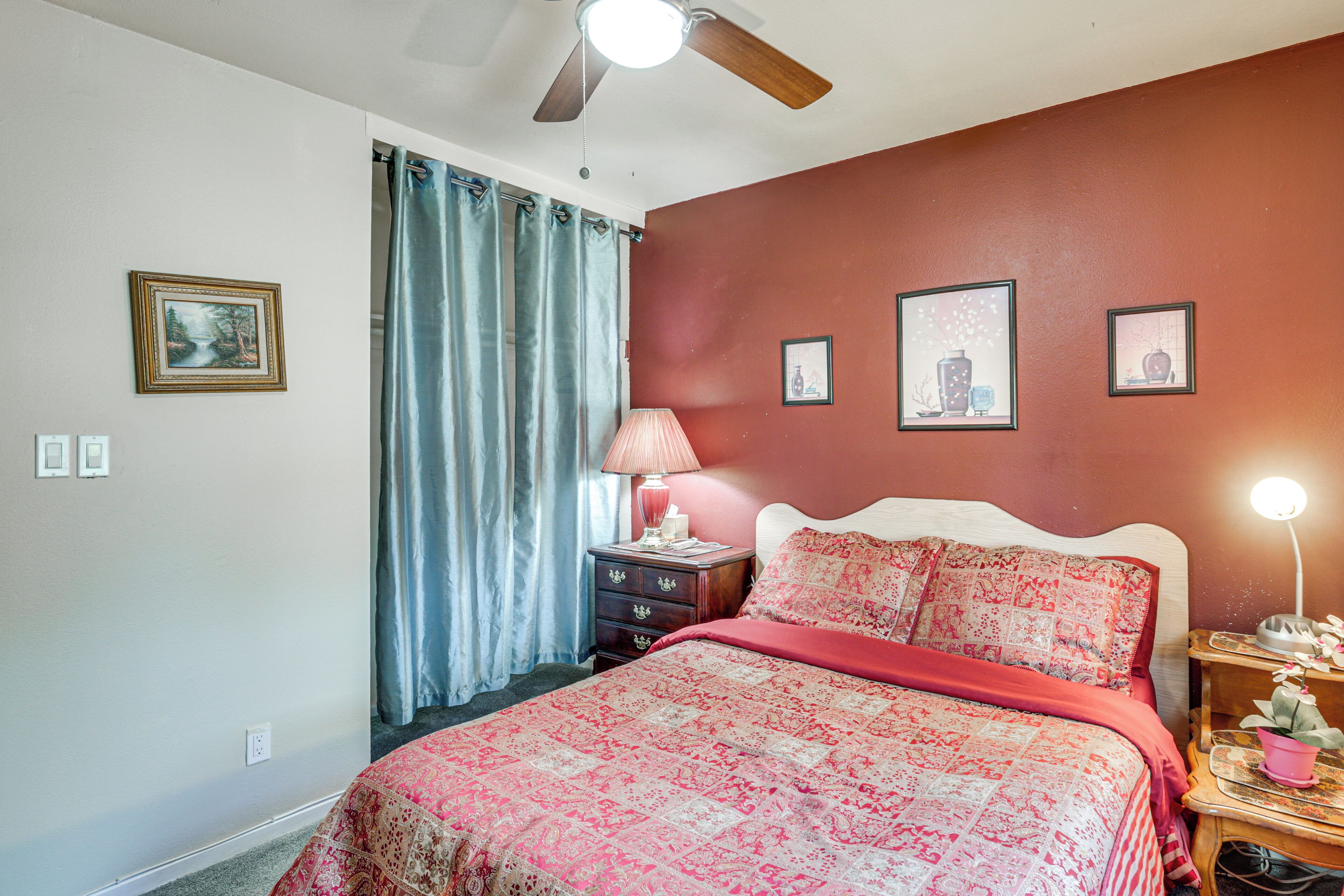 A bedroom with a bed, a nightstand, a lamp, a ceiling fan, and a window with curtains.