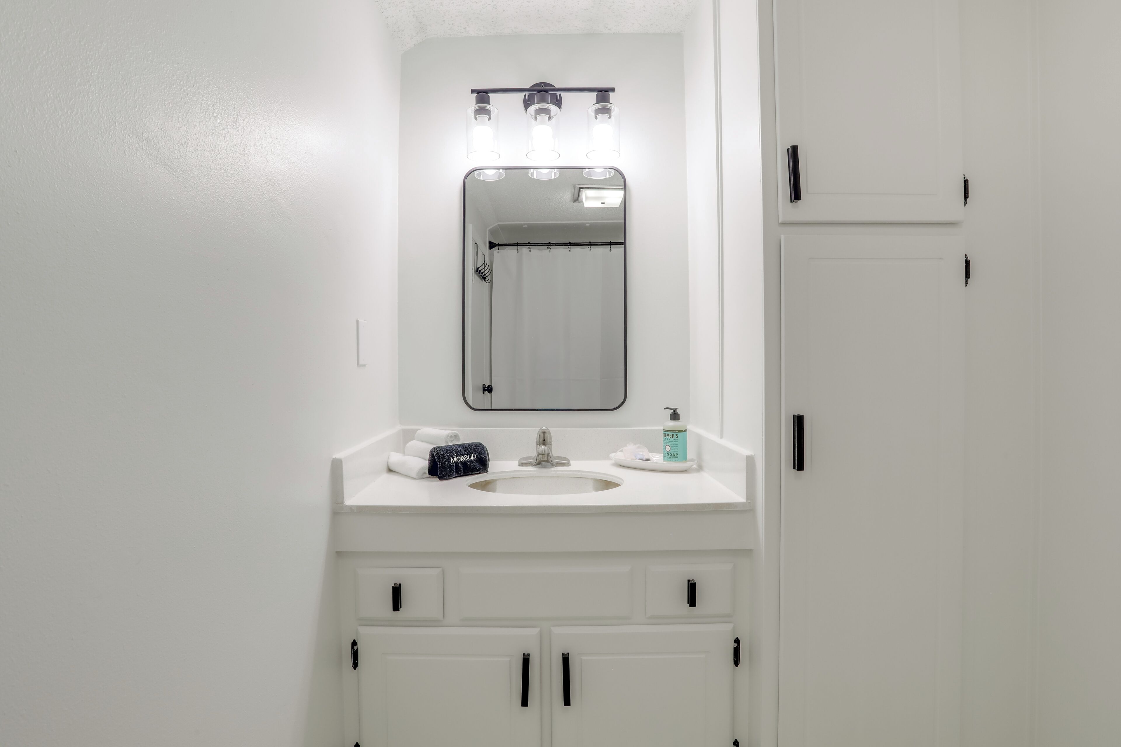 Une salle de bain avec un lavabo blanc, un miroir et des armoires.