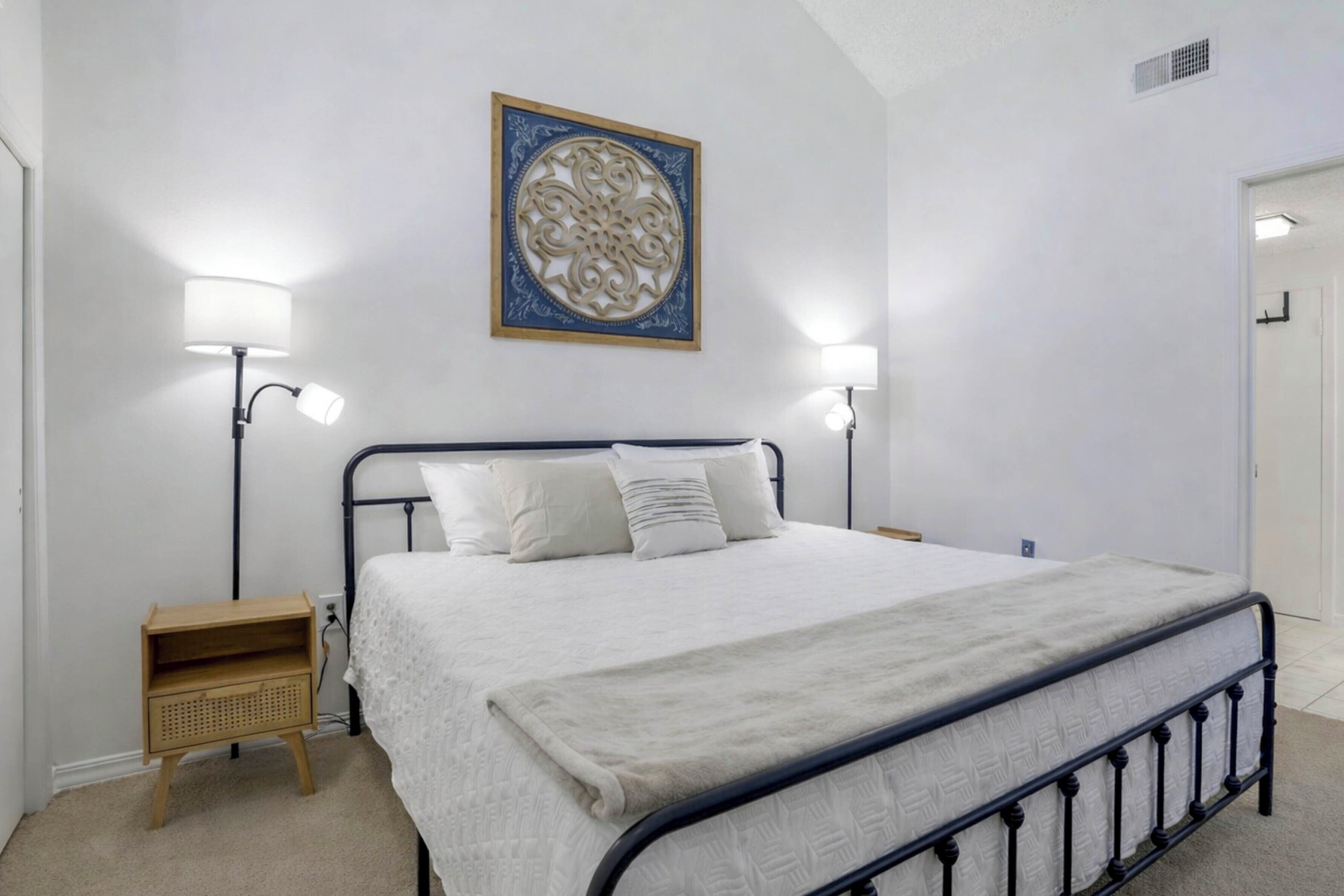 A bedroom with a bed, two bedside lamps, a nightstand, and a decorative wall piece.