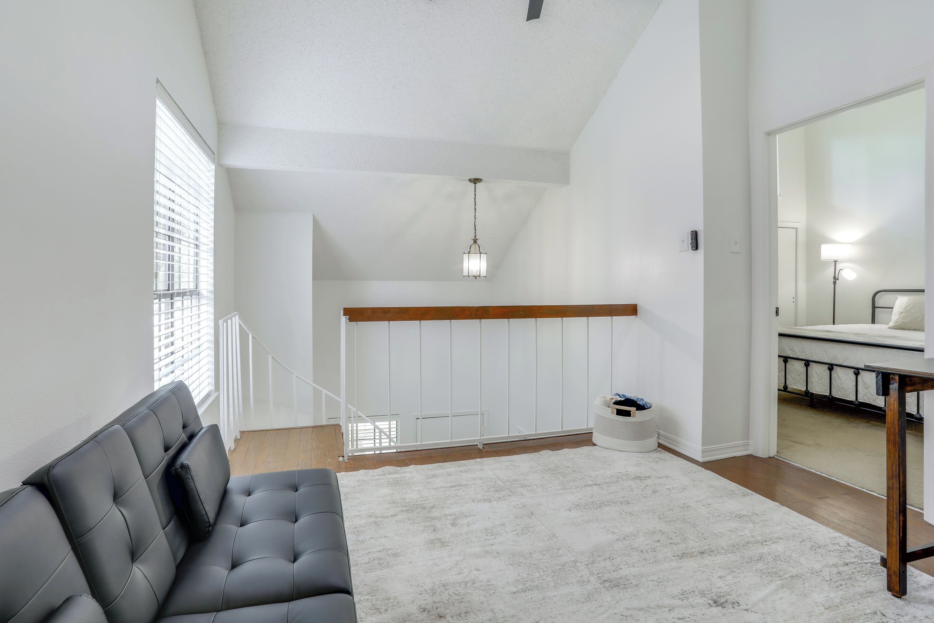 Una habitación de hotel moderna con un sofá gris, una alfombra blanca, un techo de madera y una escalera que conduce a otra habitación.