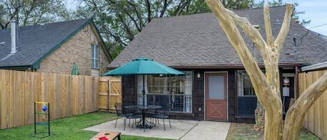 A backyard with a patio table and chairs, a green umbrella, and a wooden fence.