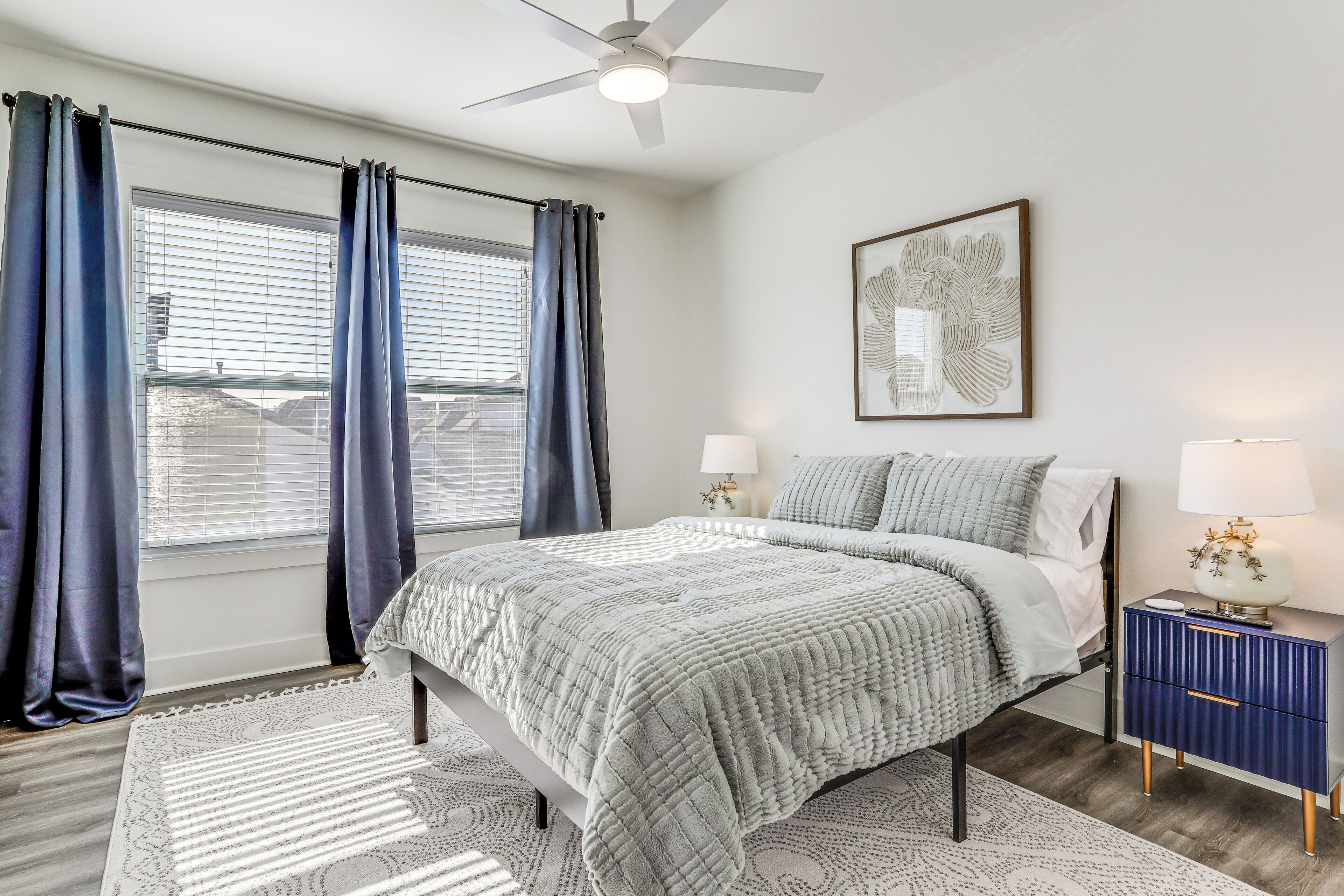 A bedroom with a bed, a nightstand, a ceiling fan, and a window with curtains.