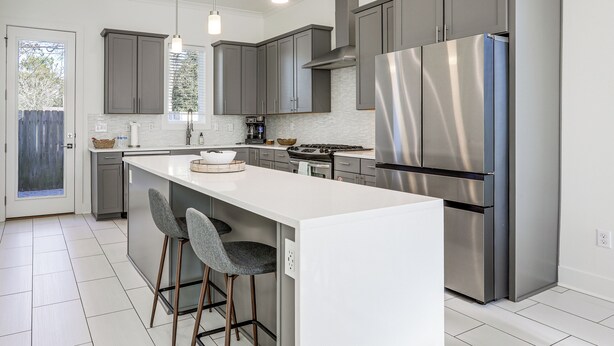 A modern kitchen with grey cabinets, stainless steel appliances, and a white island with bar stools. - Modern 3BR Retreat - Near Bluebonnet & Hospitals (Baton Rouge)