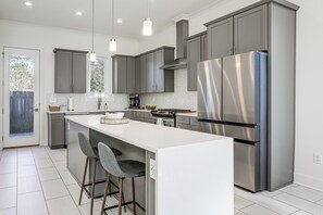 A modern kitchen with grey cabinets, stainless steel appliances, and a white island with bar stools. - Modern 3BR Retreat - Near Bluebonnet & Hospitals (Baton Rouge)