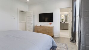A bedroom with a bed, a television, a dresser, and a bathroom visible through an open door. - Modern 3BR Retreat - Near Bluebonnet & Hospitals (Baton Rouge)