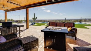 Eine Terrasse im Freien mit Korbmöbeln, einem Grill und Blick auf Pool und Berge.