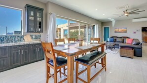 Eine moderne Küche mit dunklen Schränken, ein Essbereich mit Holzsesseln, eine Couch und ein Deckenventilator.