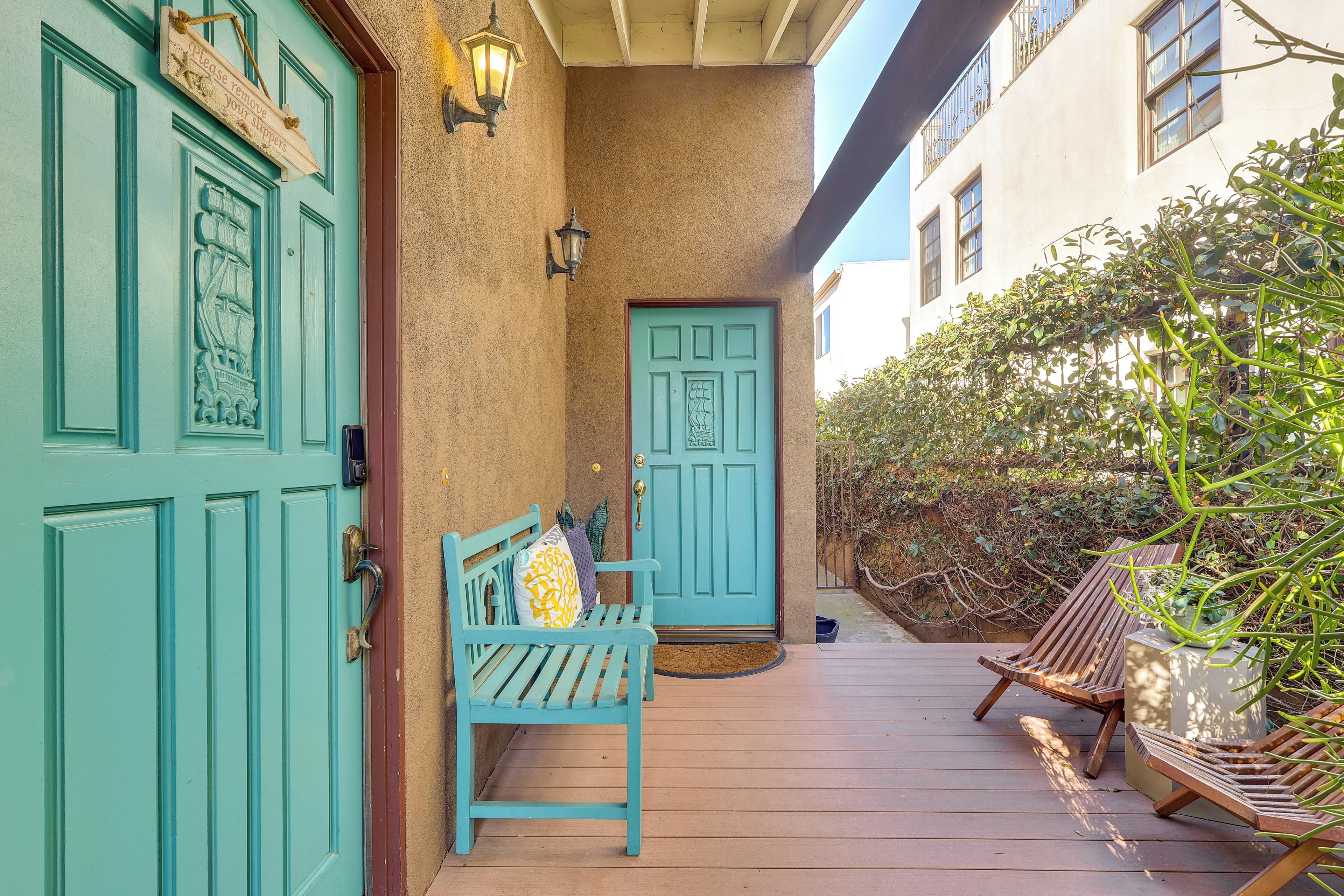 A wooden deck with a bench and two chairs, a turquoise door, and a wall-mounted sign.