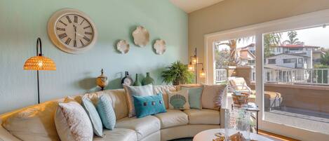 A living room with a curved white sofa, a round coffee table, a wall clock, and a large window with a view of houses.