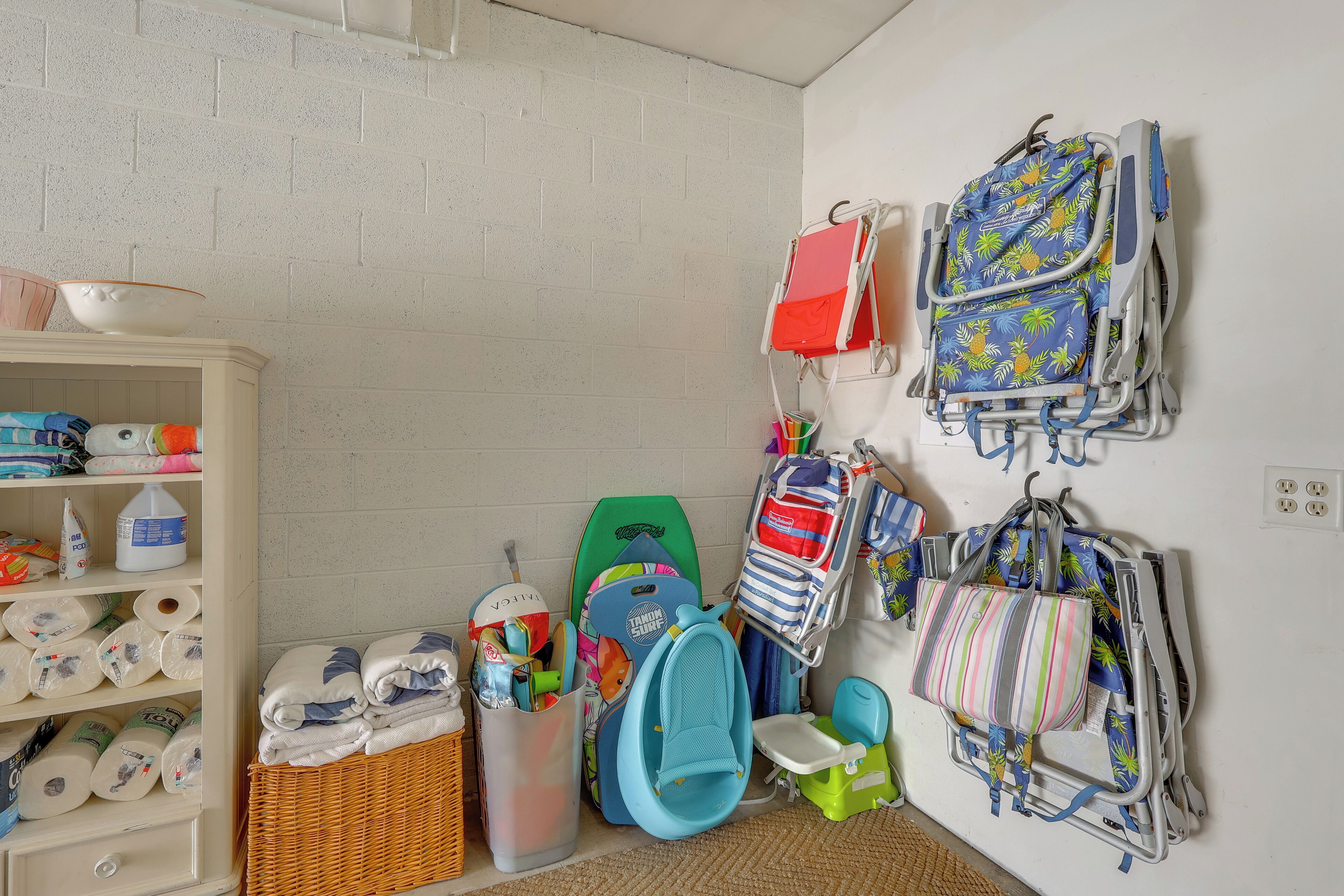 A room with a white brick wall, a white cabinet with baby supplies, and multiple children's backpacks and toys.