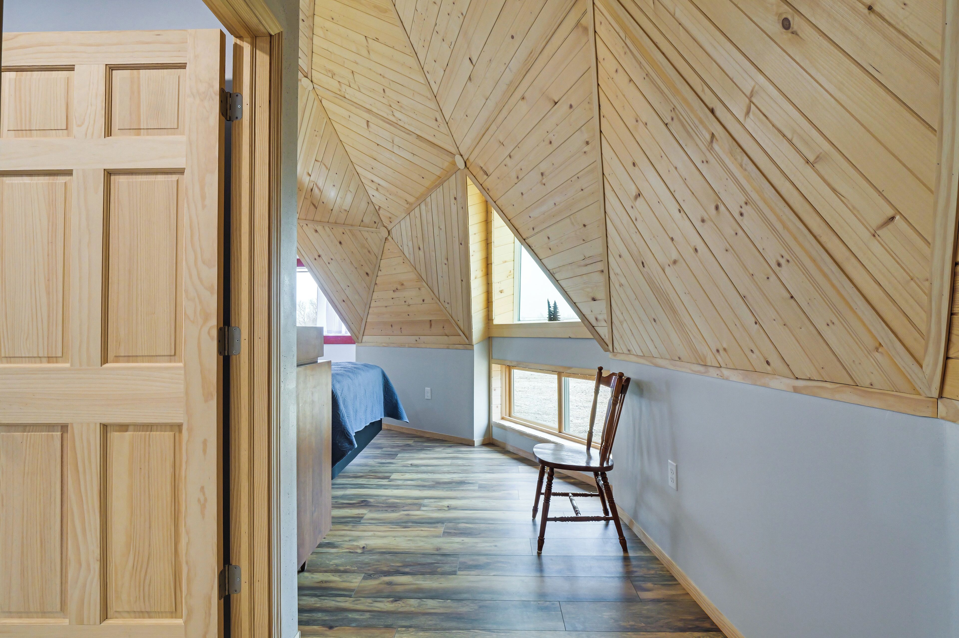Une pièce avec un plafond en pente, un plancher en bois, un lit et une chaise.