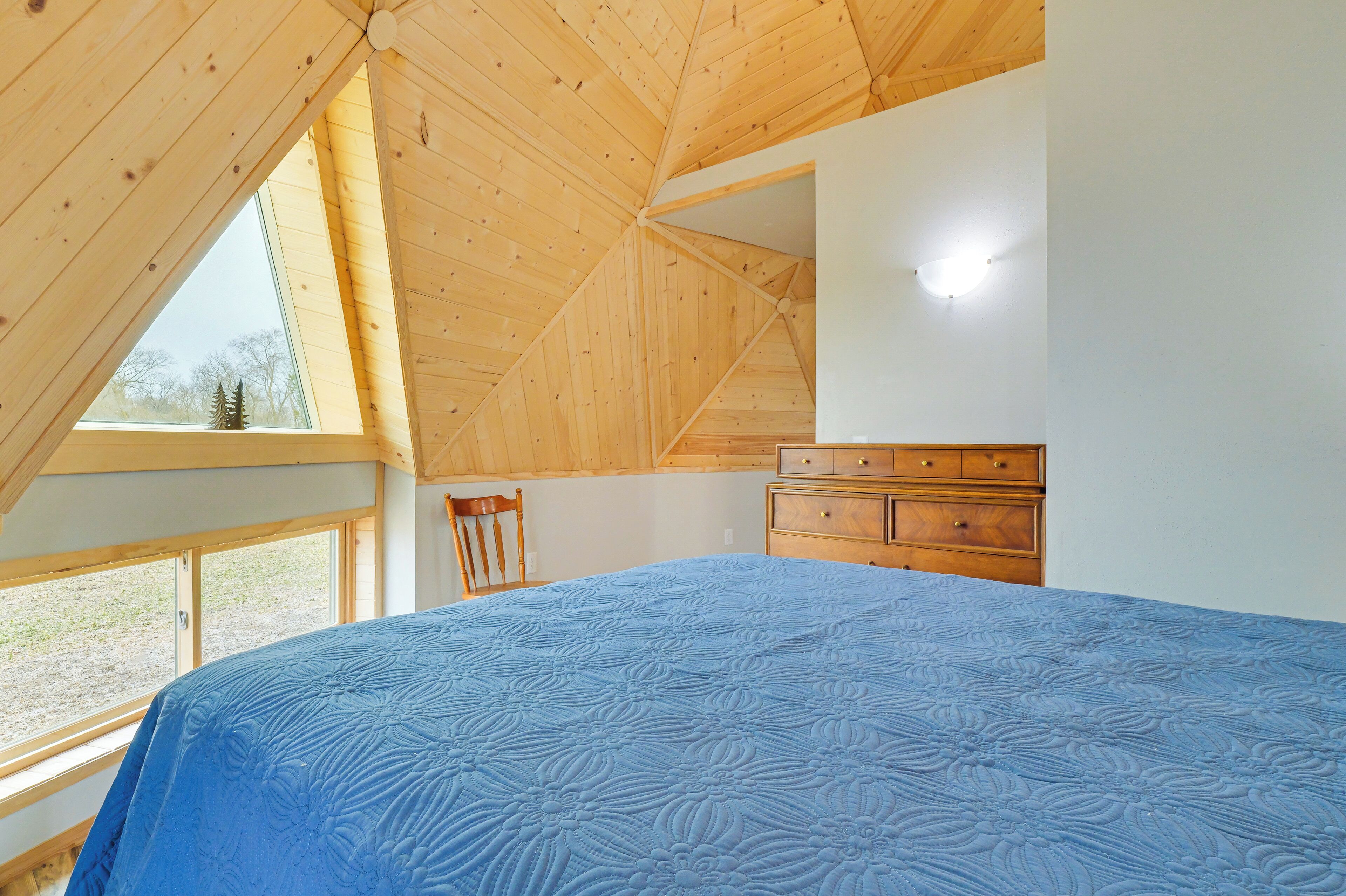 Une chambre avec un grand lit, un plafond en bois, une commode et une fenêtre.