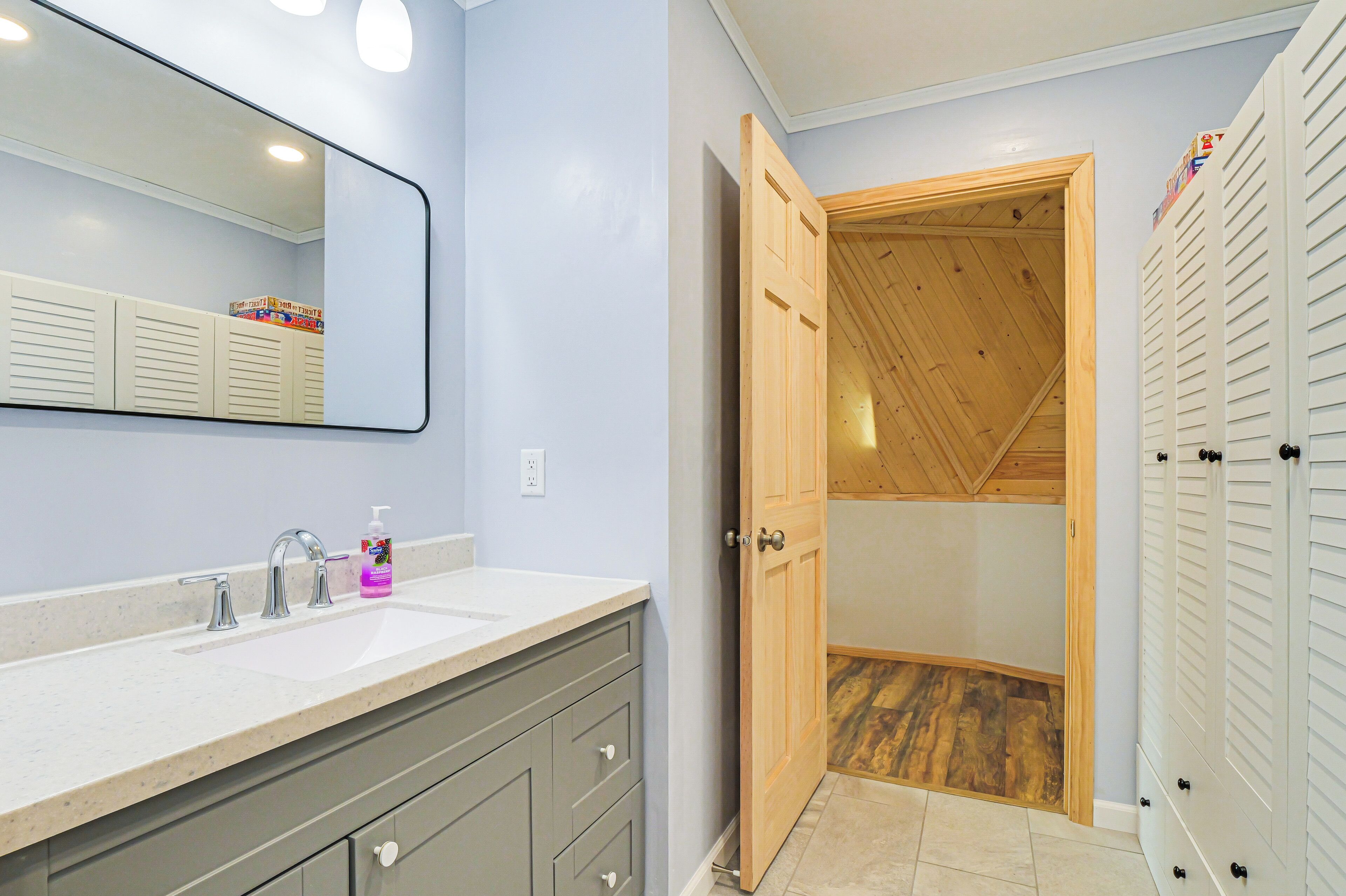 A bathroom with a sink, mirror, and wooden door leading to a shower area.