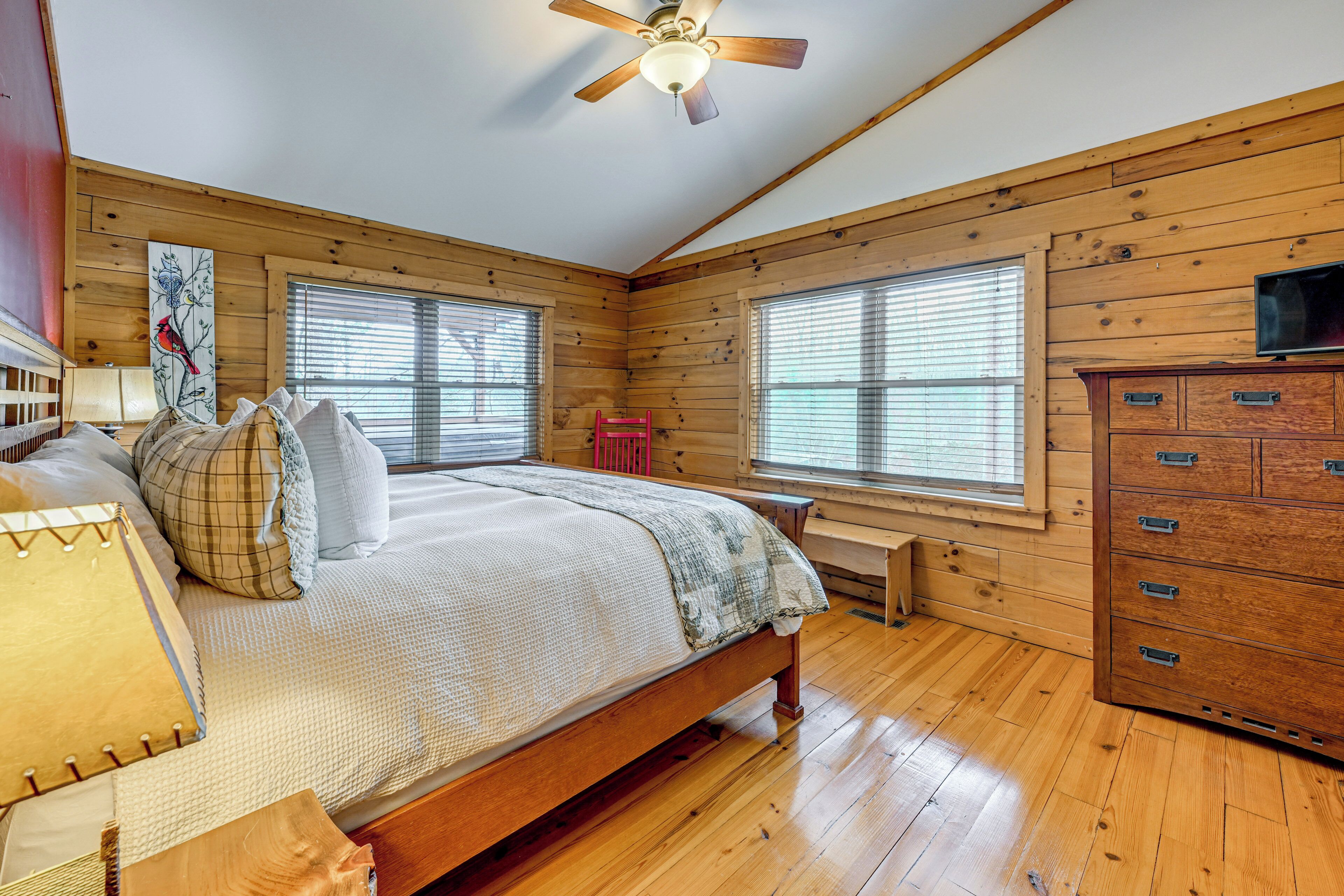 A wooden-paneled bedroom with a bed, dresser, and a ceiling fan.