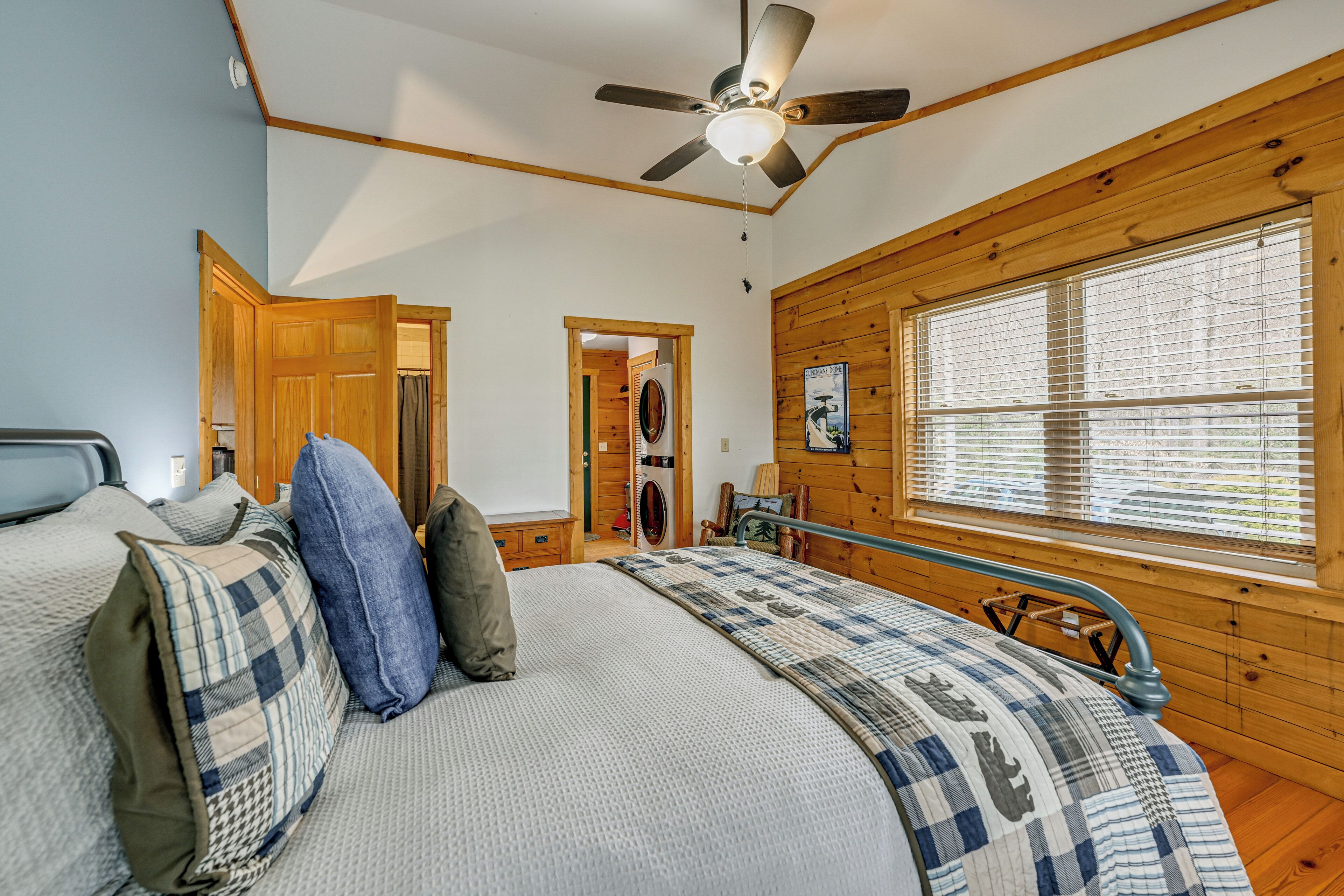 A bedroom with a bed, a ceiling fan, wooden walls, a window, and a door.