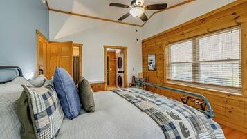 A bedroom with a bed, a ceiling fan, wooden walls, a window, and a door.
