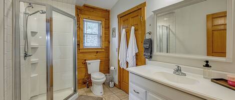 A bathroom with a glass shower enclosure, a toilet, a sink, and a large mirror.