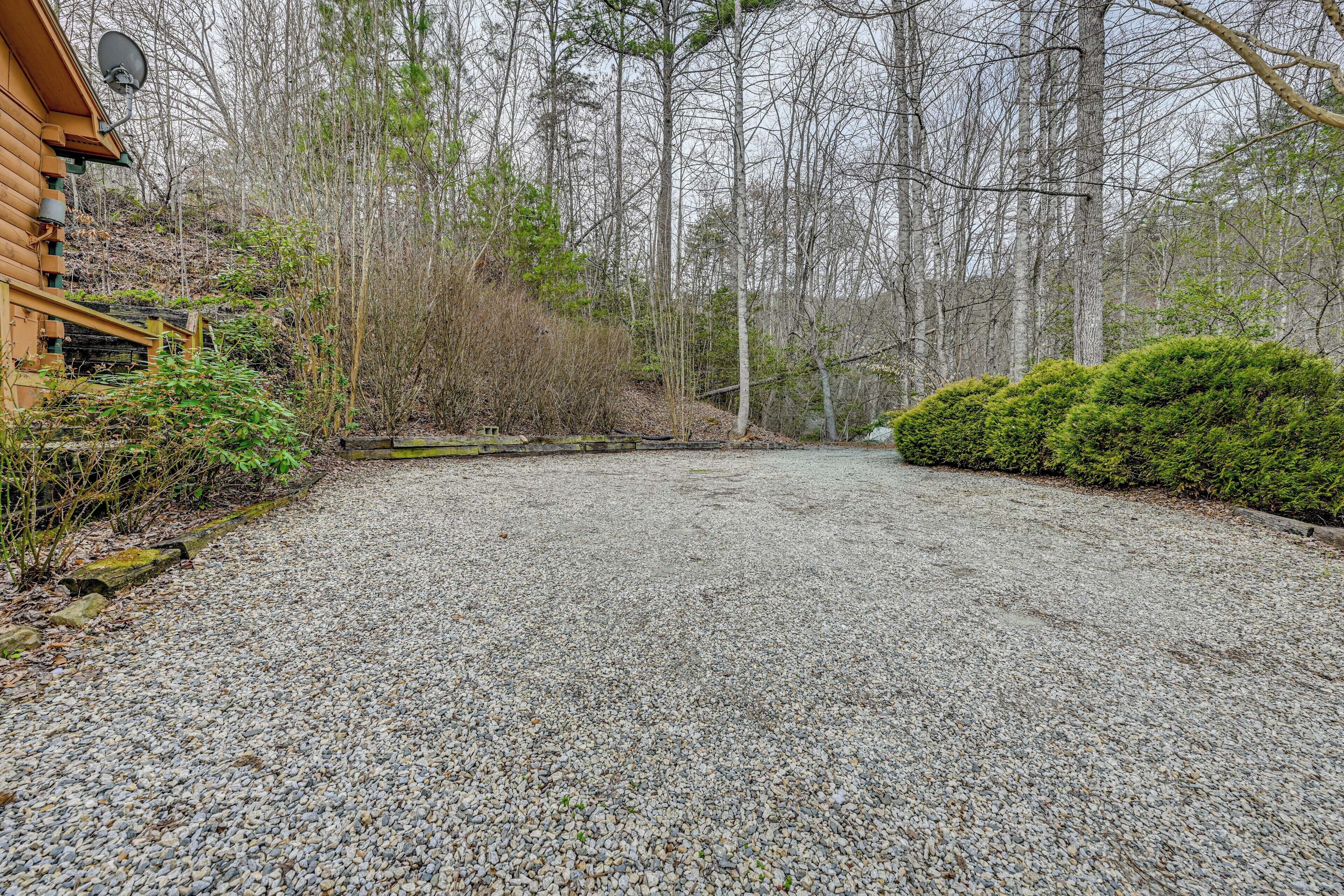 A gravel driveway leading to a wooden cabin with a satellite dish, surrounded by dense forest.
