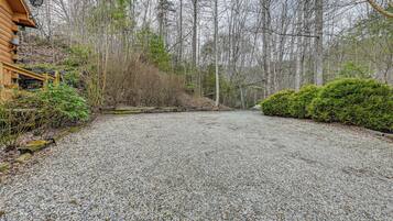 A gravel driveway leading to a wooden cabin with a satellite dish, surrounded by dense forest.