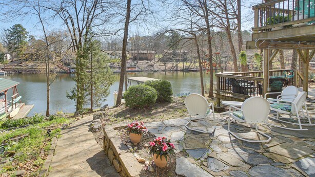 Un patio junto al lago con suelo de piedra, plantas en macetas y mobiliario de exterior.