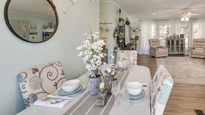 Un comedor con una mesa larga dispuesta para cuatro personas, un espejo y un jarrón con flores blancas.