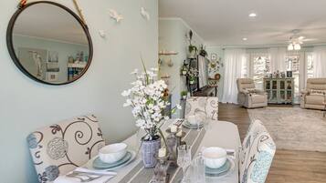 A dining area with a long table set for four, a mirror, and a vase with white flowers.