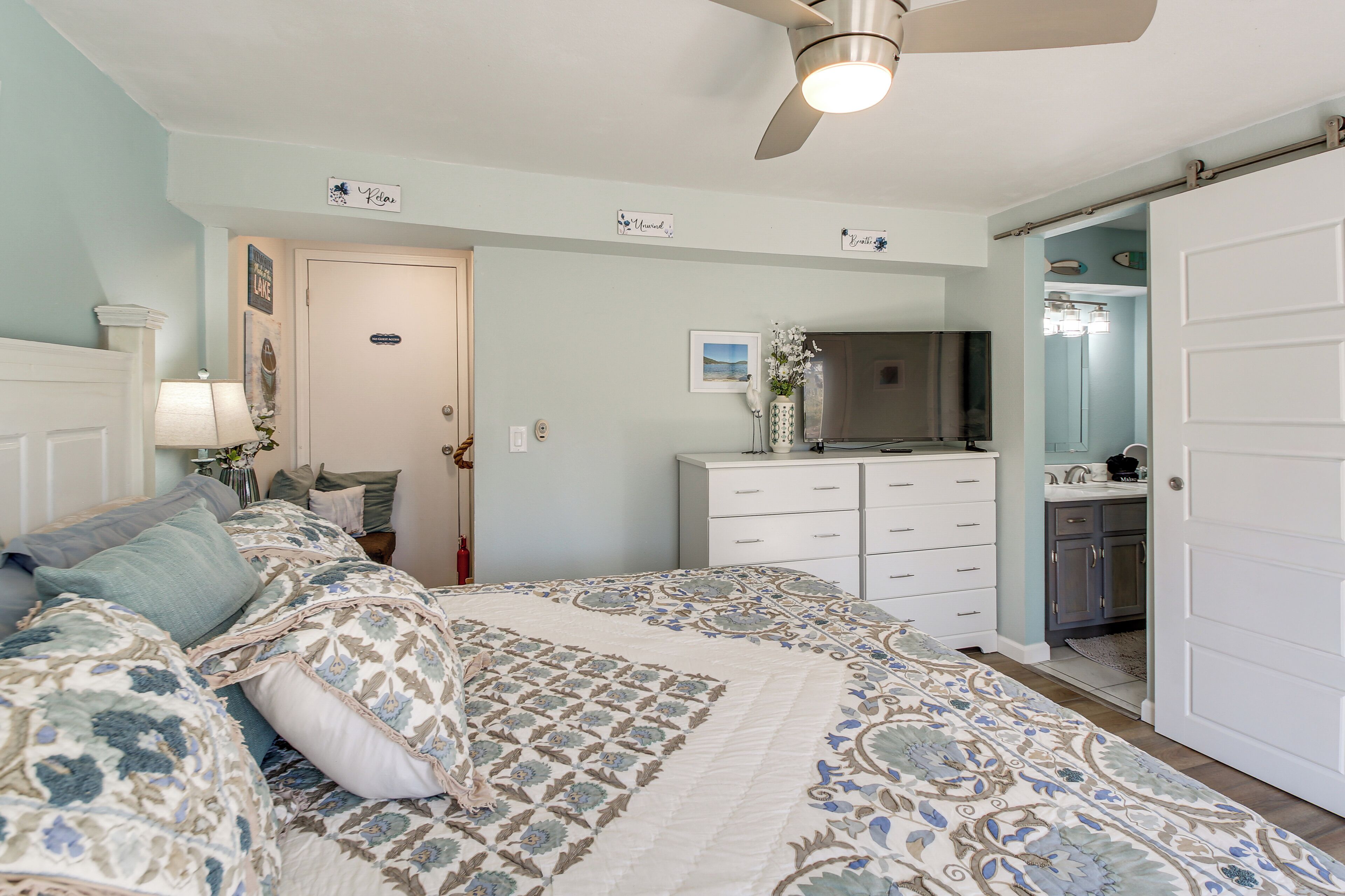 A bedroom with a bed, a dresser, a television, and a bathroom door.
