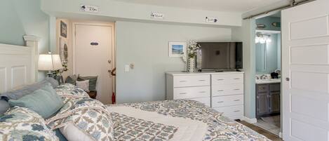 A bedroom with a bed, a dresser, a television, and a bathroom door.
