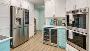 Una cocina con electrodomésticos de acero inoxidable, armarios blancos, una encimera azul y un enfriador de vino empotrado.